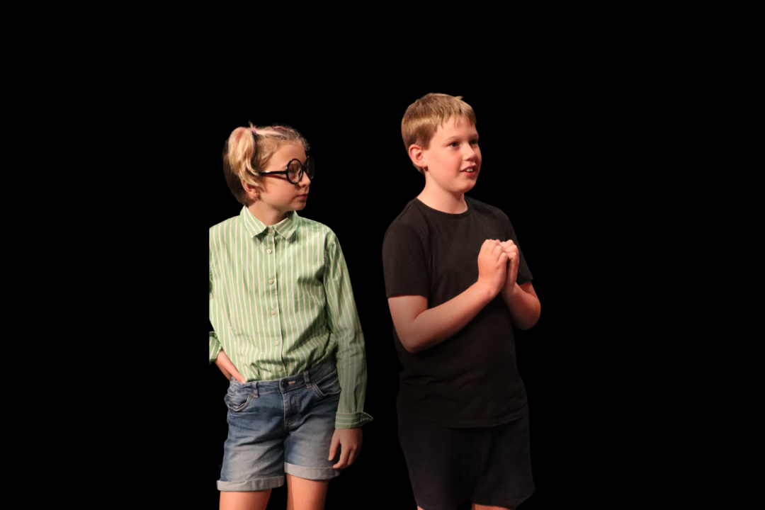 Young boy staring off into the distance with young girl looking at the boy curiously from behind. 