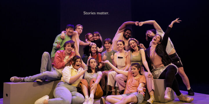 Youth arts participants posing in a group on stage.